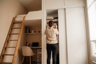 Femme rangeant des textiles dans une armoire encastrée dans un studio parisien avec mezzanine, optimisant l'espace vertical